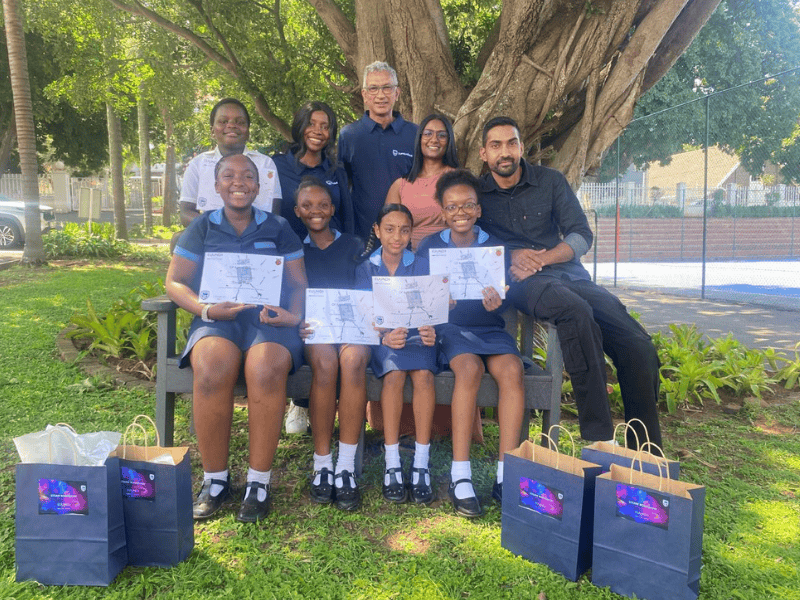 A group of students sit under a tree with their teachers