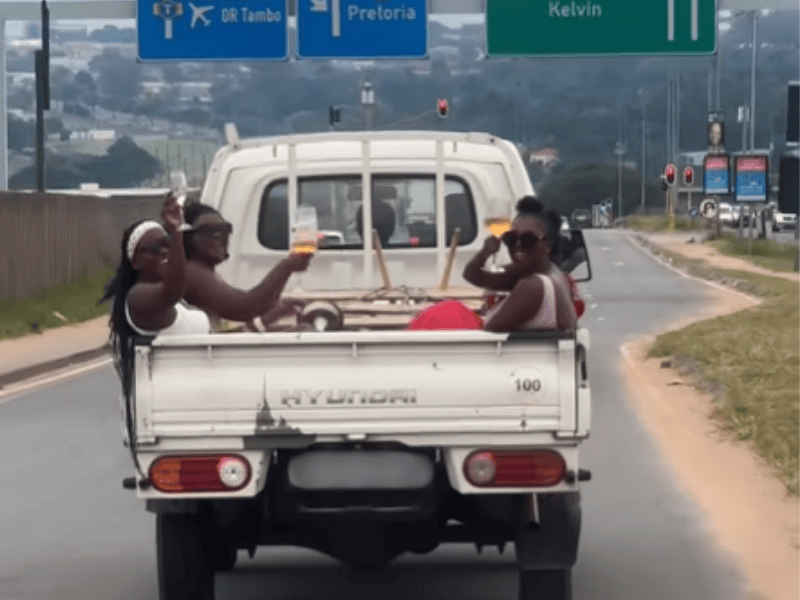 A group of women seated at the back of a bakkie drinking wine