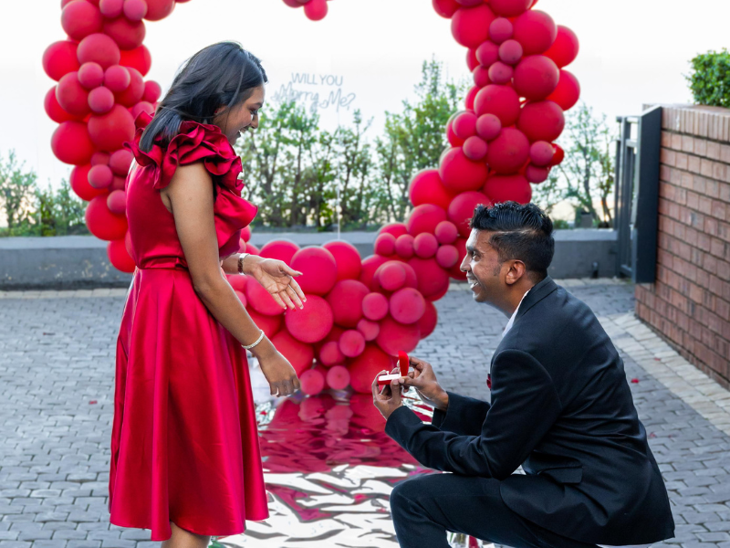 A guy proposes to his girlfriend with red balloons in the background