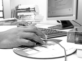 A hand using a mouse in front of a desktop computer