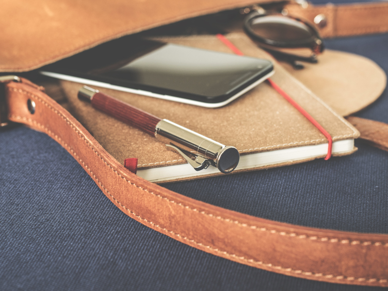 A handbag that has a smartphone, notebook, sunglasses and pen