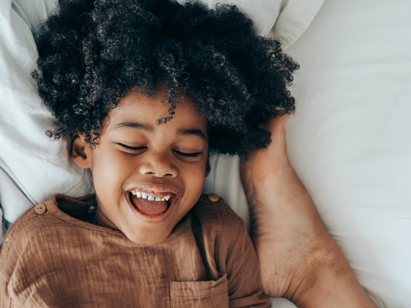 A happy African American boy lying on the bed and laughing