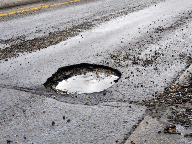 A large pothole filled with water on an asphalt road