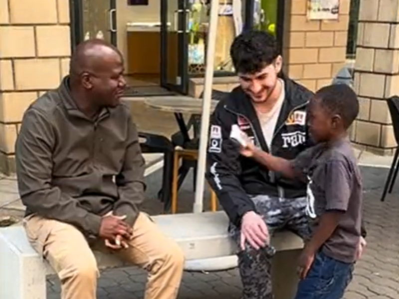 A little boy hands cash to a man sitting on a bench