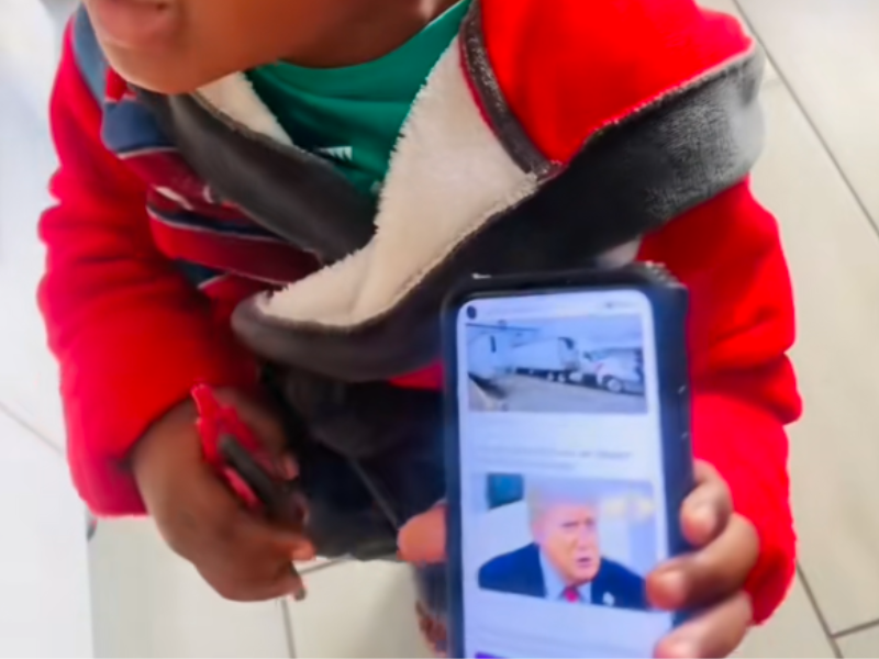 A little boy points to a picture of Donald Trump on the phone