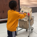 A little boy pushes a trolley filled with groceries out of a supermarket