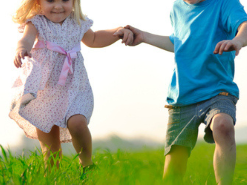 A little girl and boy holding hands and running through a field