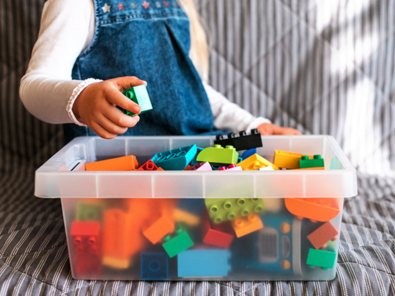 A little girl cleaning up the toy box at home