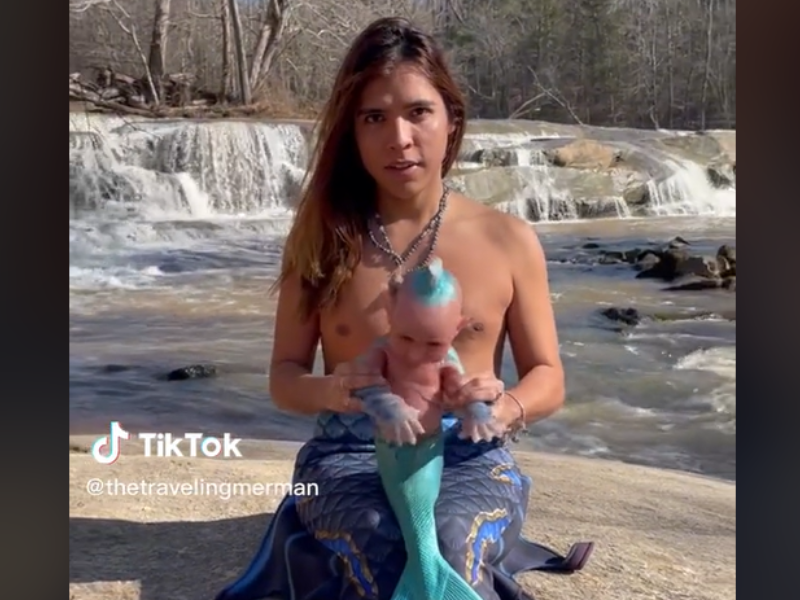 A man dressed as a merman with a baby doll