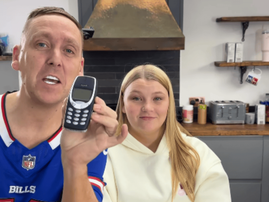 A man holds a Nokia 3310 in hand while his daughter sits nearby