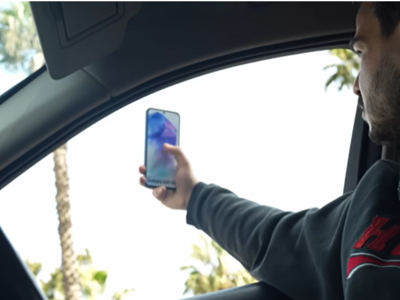 A man holds his phone out a car window