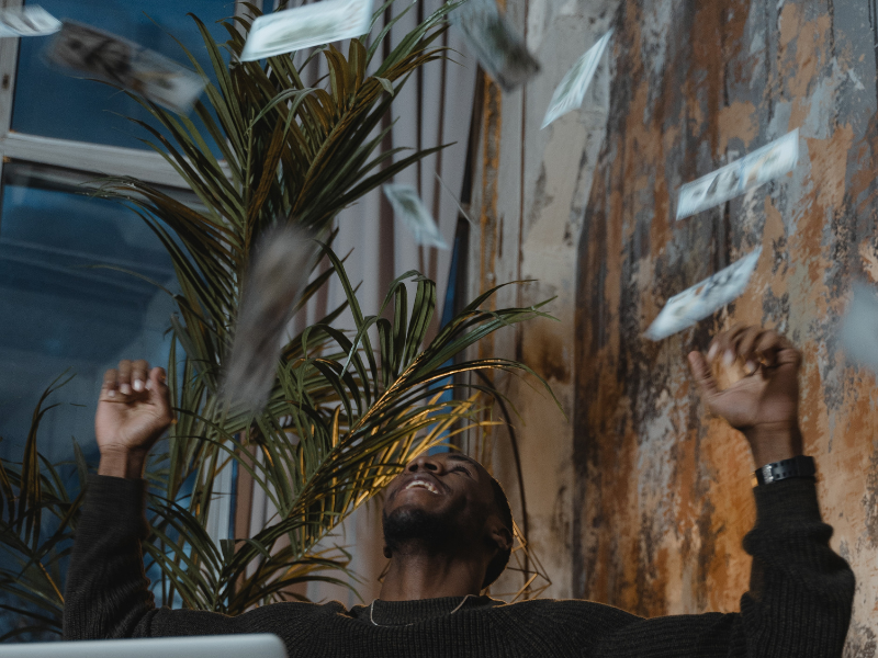 A man in a sweater celebrating with money in the air