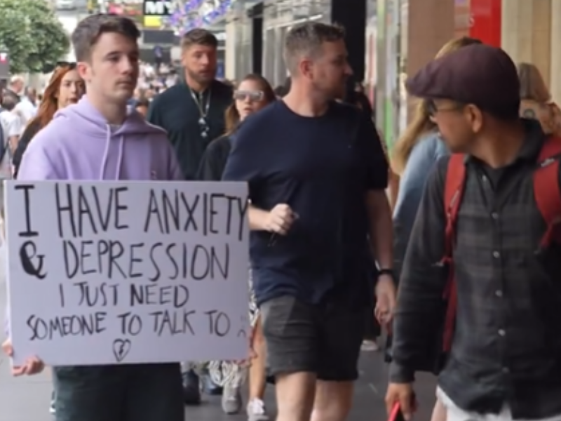 A man is standing in a busy place with a placard