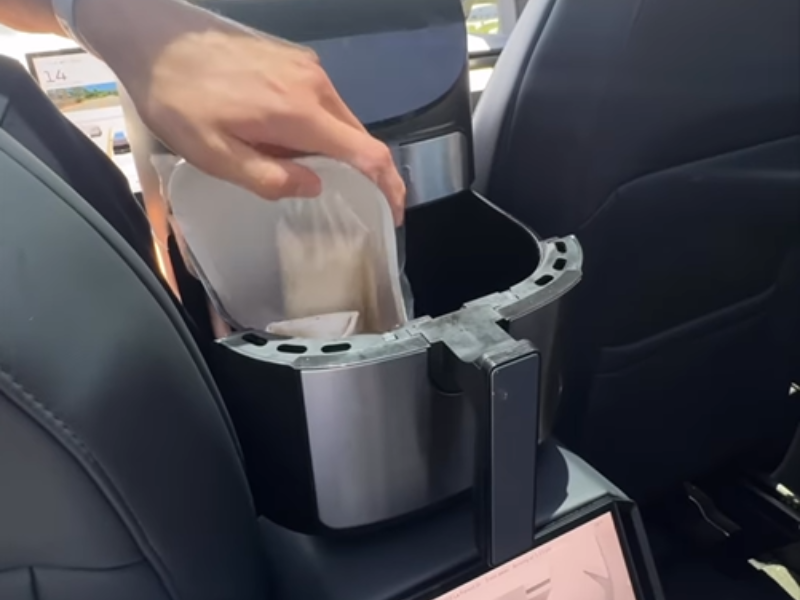A driver places food inside an air fryer inside his vehicle