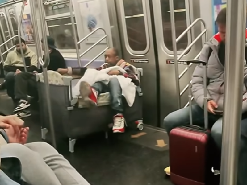 A man sleeps inside a baby crib in a train
