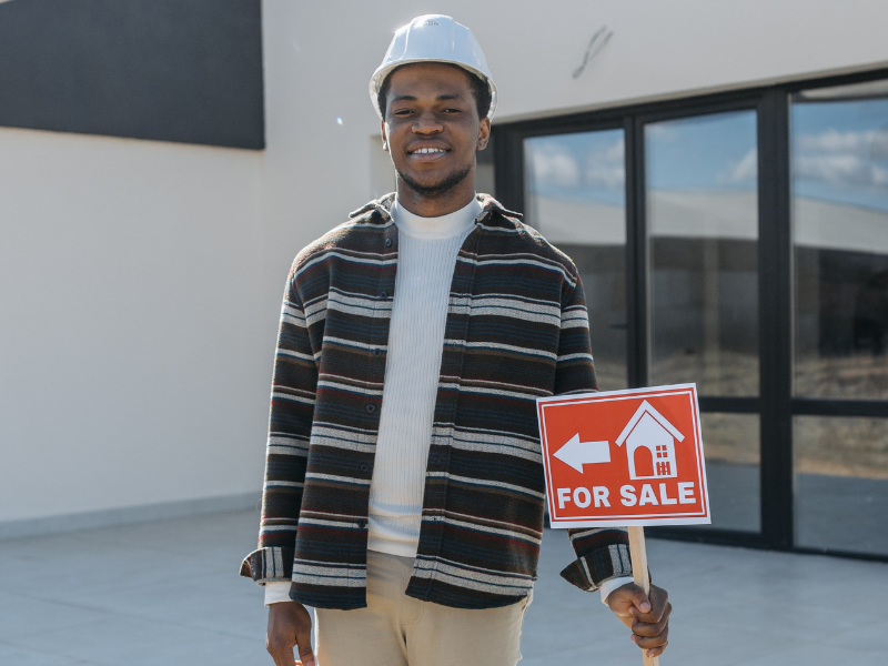 A man wearing a hard hat holding a sign outside a house