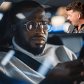 A man wearing glasses looks at his smartphone inside car