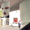 A man wears a balaclava in his car talking to a security guard on the road
