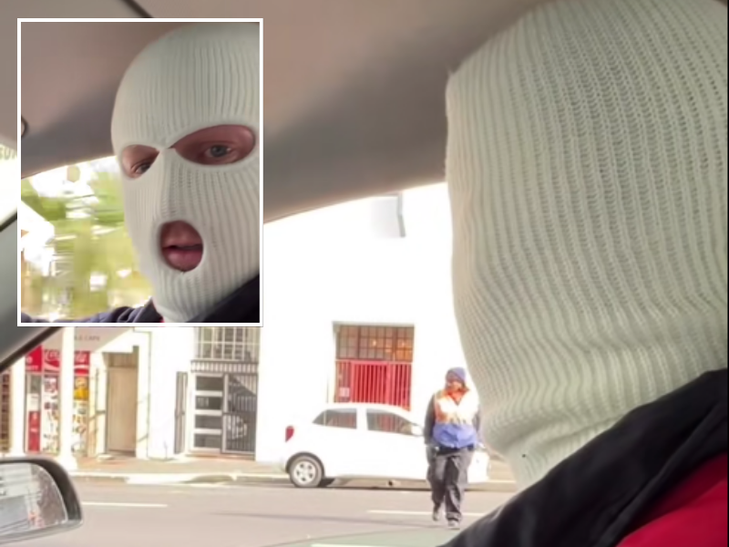 A man wears a balaclava in his car talking to a security guard on the road