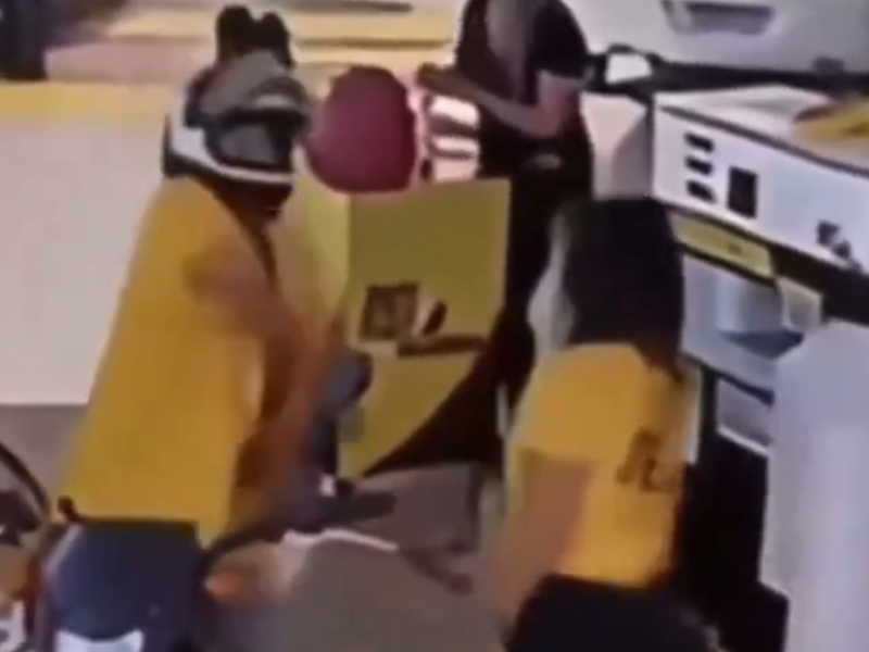 A man with a biker helmet scares a petrol attendant