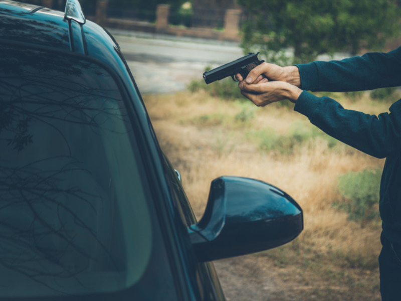 A man with a hand gun pointing it at a driver inside a car