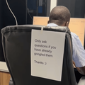 A man works at his desk and has a note on his chair to avoid disturbance