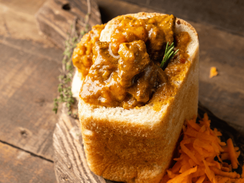 A meat bunny chow on a wooden surface with a carrot salad