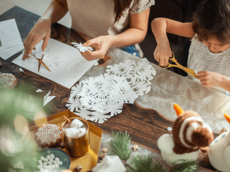 A mother and daughter cutting snowflakes out of paper