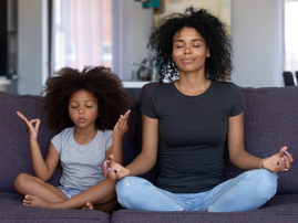 A mindful mother and daughter engage in a yoga pose on the couch