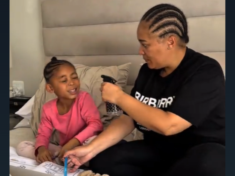 A mother holds a spray bottle in hand and points it at her daughter while they do homework