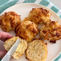 A person butters a cheesy scone on a plate