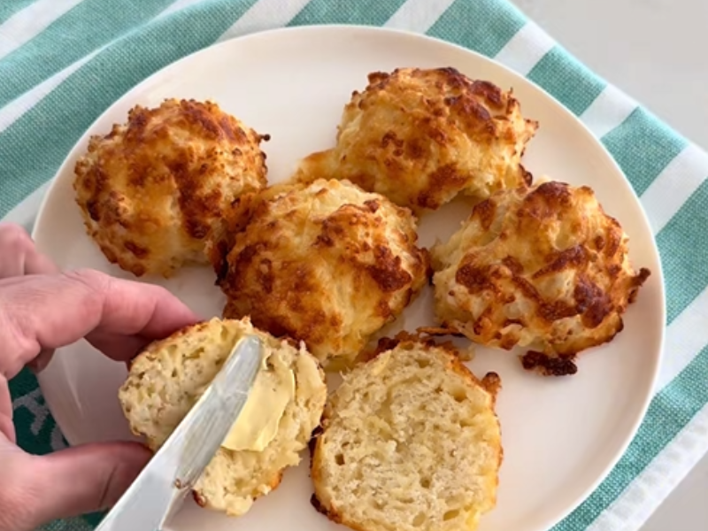 A person butters a cheesy scone on a plate