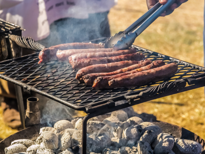 A person cooking sausages on a braai stand