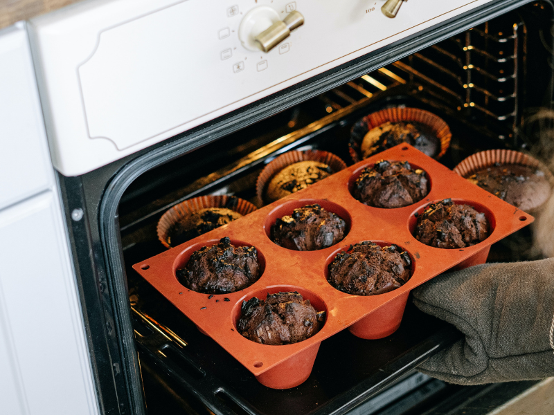 A person holding a baking tray of muffins out of the oven
