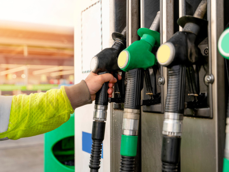 A person holding the petrol and diesel nozzles of the dispenser at a petrol station