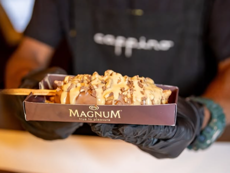 A person holds a Magnum ice cream on a box loaded with other chocolate treats