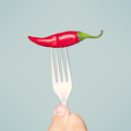 A person holds a fork with a red chilli on it