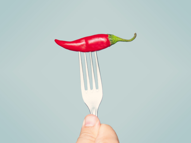 A person holds a fork with a red chilli on it