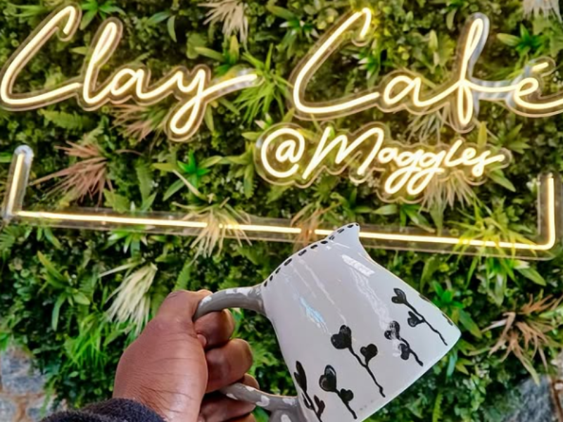 A person holds a handcrafted milk jug against a light sign