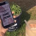 A person holds a phone showing a poster to Durban cake picnic and ice coffee