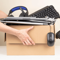 A person picks up a box with used headphones a keyboard and laptop