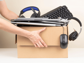 A person picks up a box with used headphones a keyboard and laptop