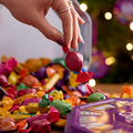 A person picks up a wrapped candy from tin of Quality Street