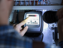 A person points at the electricity meter reading on their power box