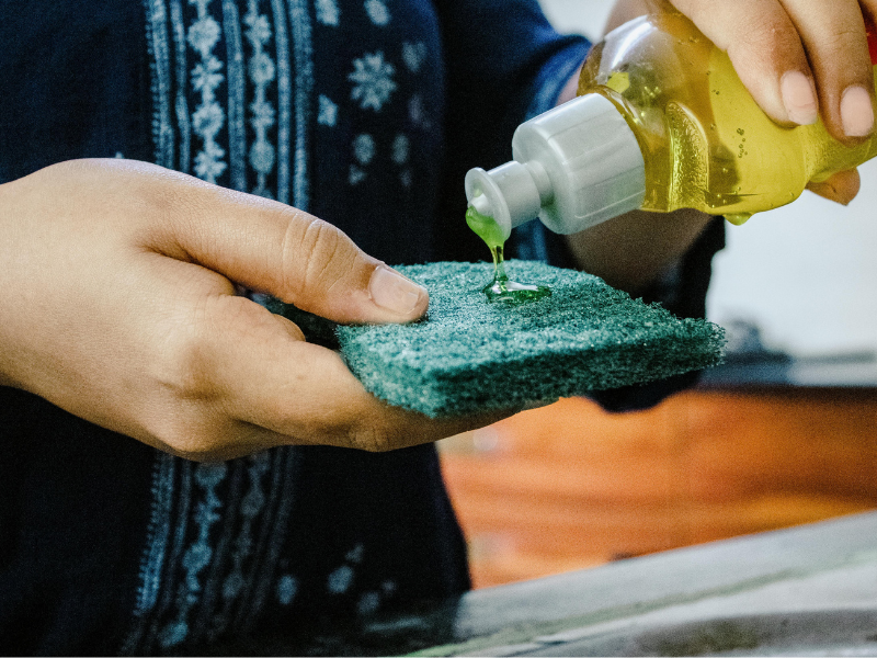 A person pouring dishwashing liquid onto a sponge