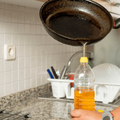 A person pouring used cooking oil from a frying pan into a plastic bottle