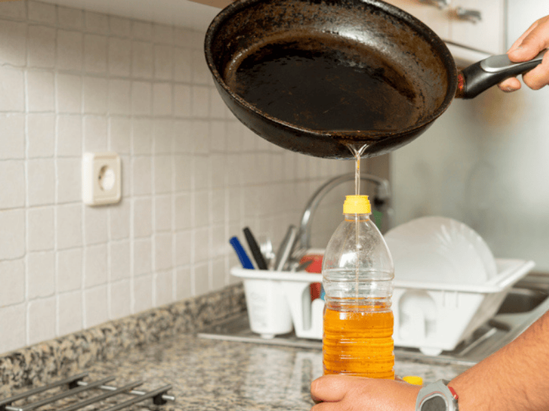 A person pouring used cooking oil from a frying pan into a plastic bottle