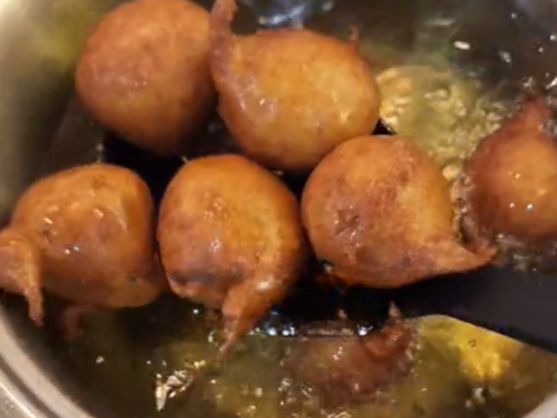 A person removes fried snack from hot oil in a pot