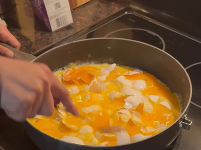 A person smashes eggs in a frying pan on the stove top