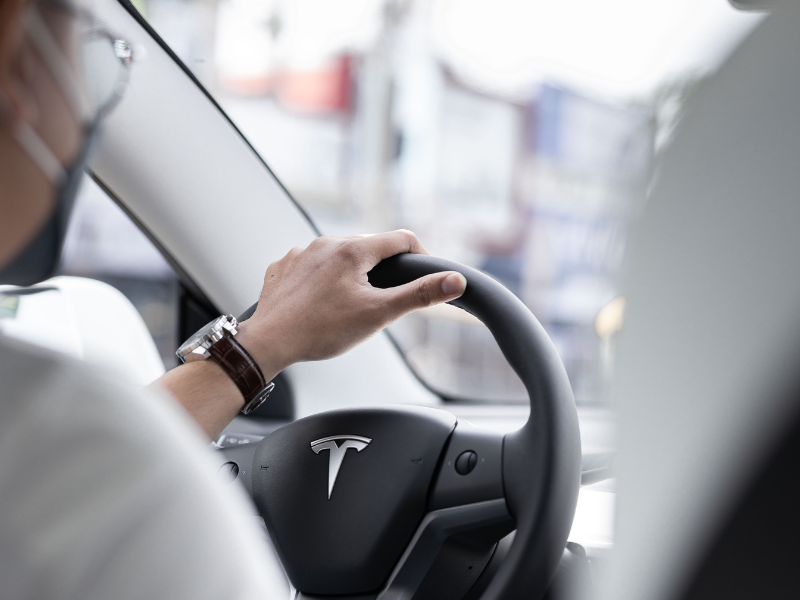 A person wearing a face mask driving a tesla